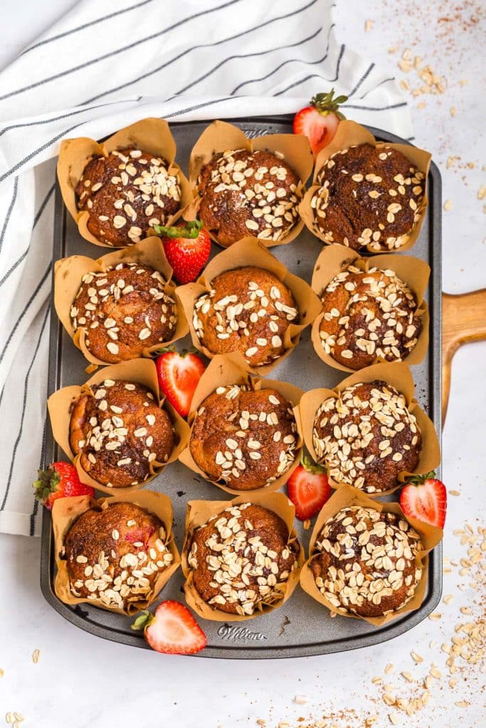 baked strawberry muffins, still in the pan. There are oats sprinkled on the counter and strawberries on the pan