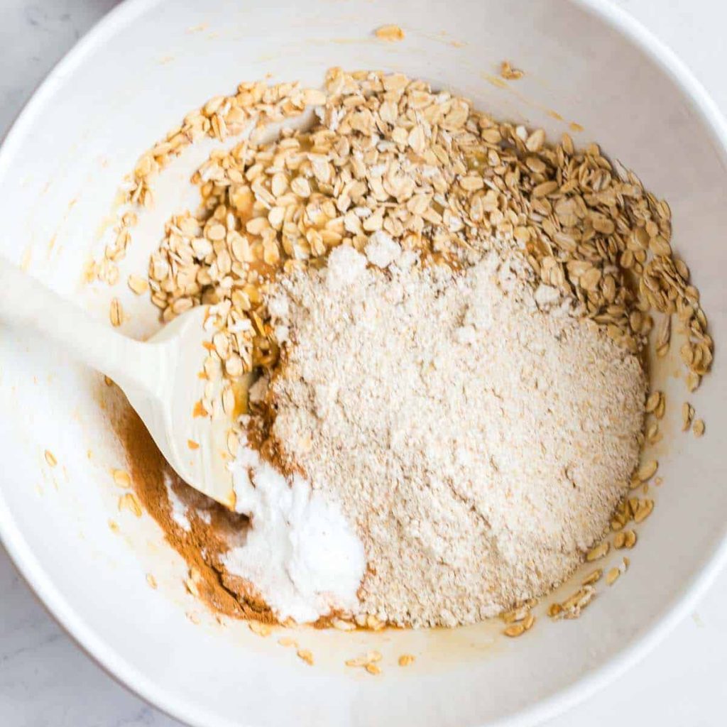 oats and flour in a white bowl. White spoon inside bowl on the left side. 