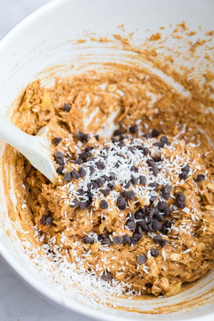 image of chocolate chips and shredded coconut being mixed into the batter, in a white bowl