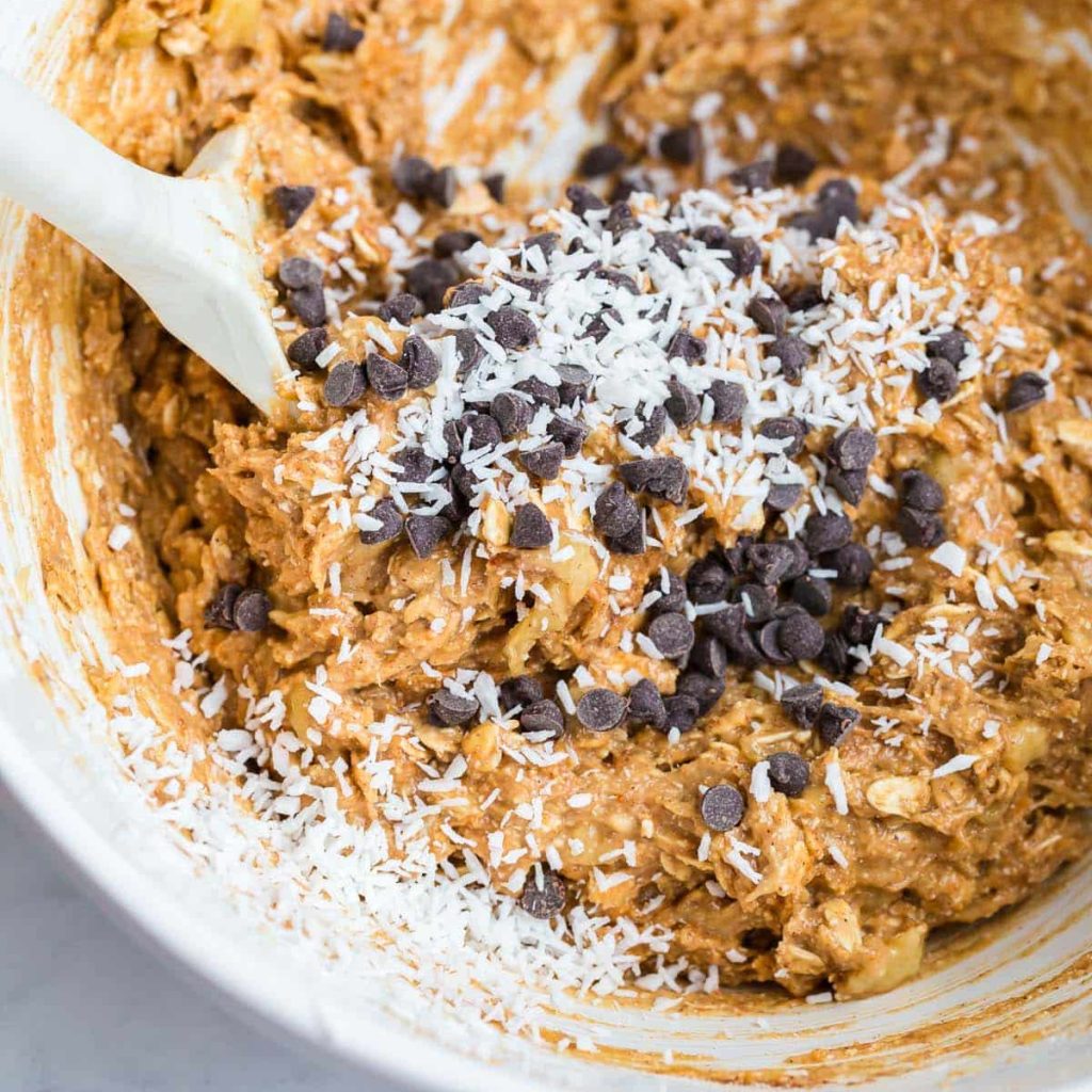 image of chocolate chips and shredded coconut being mixed into the batter, in a white bowl