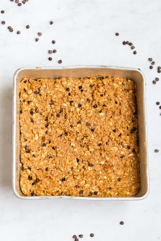 batter for this recipe poured into a square steel pan, there are chocolate chips in the background on the white counter