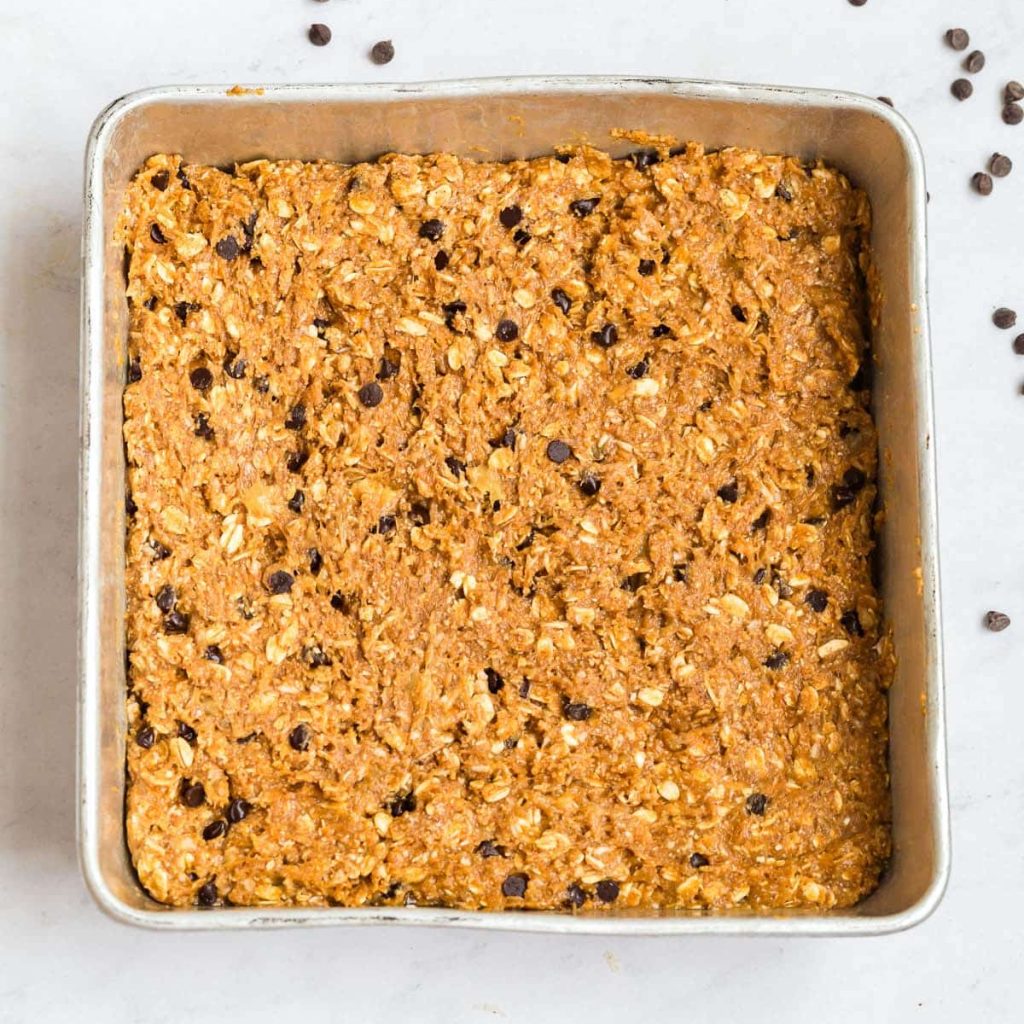 batter for this recipe poured into a square steel pan, there are chocolate chips in the background on the white counter.