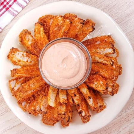 top down view of a white plate with a baked blooming onion and a clear bowl of dip in the middle