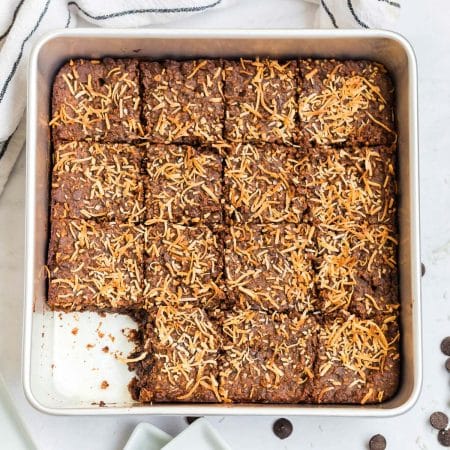 top down view of a cooked pan of black bean brownies with toasted coconut on top. One brownie is missing.