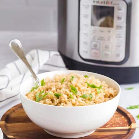 coconut rice in a white bowl with cut green onions on top. In the background is an Instant Pot Pressure Cooker.