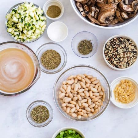 top down view of ingredients needed for mushroom and wild rice soup in small bowls on a white counter
