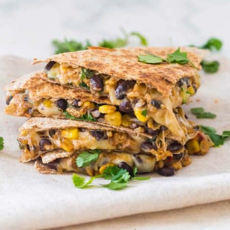 view of four slices of quesadilla stacked on top of one another. Whole wheat tortillas filled with corn, black beans, zucchini, rice, and melted cheese. Garnished with fresh cilantro.