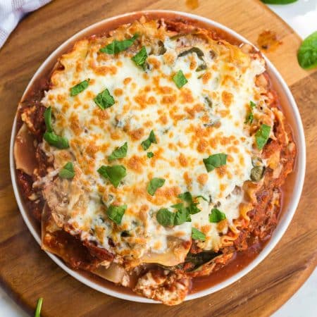 top down view of cooked lasagna in a round pan. Melted and browned cheese on top, garnished with fresh basil