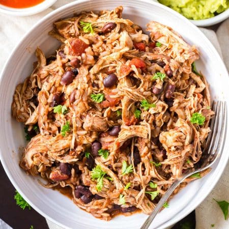 top down image of chicken burrito bowl. You can see shredded chicken, black beans, chunks of tomatoes, and pieces of parsley on top.
