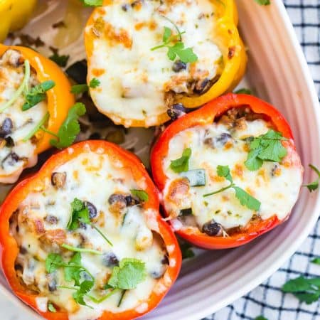 top down image of vegetarian stuffed peppers with black beans and rice, with browned cheese on top