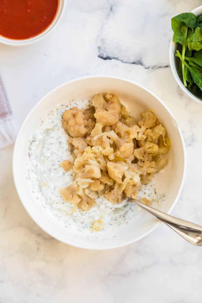 bowl with cottage cheese and greek yogurt that have been blended together with spices. topping the mixture is cooked cauliflower to be mixed in.