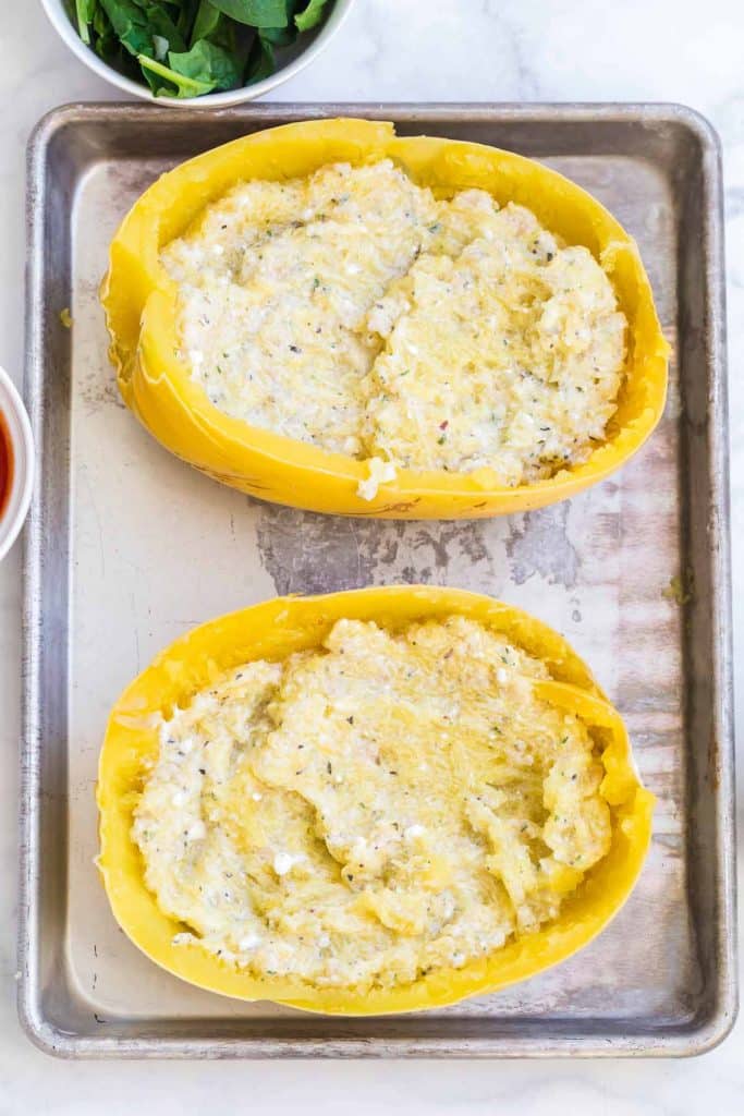 baking sheet with spaghetti squash halves filled with cottage cheese, greek yogurt, cauliflower and spices mixture
