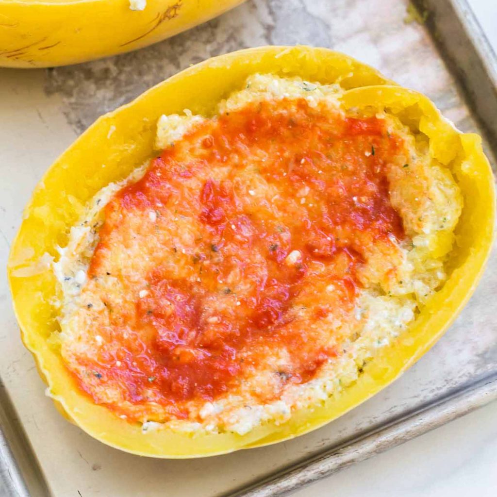 baking sheet with spaghetti squash halves, filled with cottage cheese greek yogurt mixture, and topped with tomato sauce