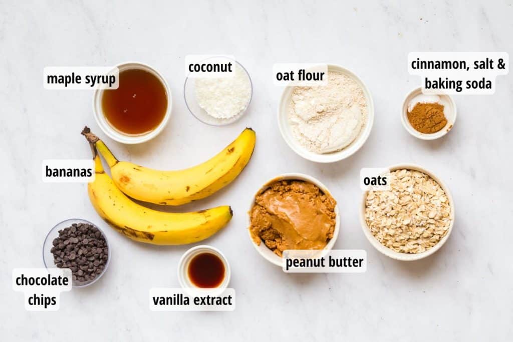 labeled ingredients for peanut butter banana oatmeal bars recipe. ingredients are on a white countertop, and in white bowls