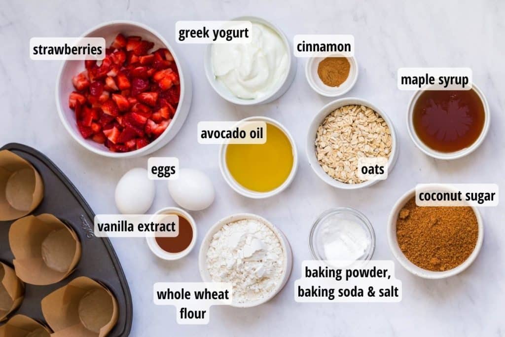 A white marbled counter with labeled ingredients needed to make healthy strawberry muffins.