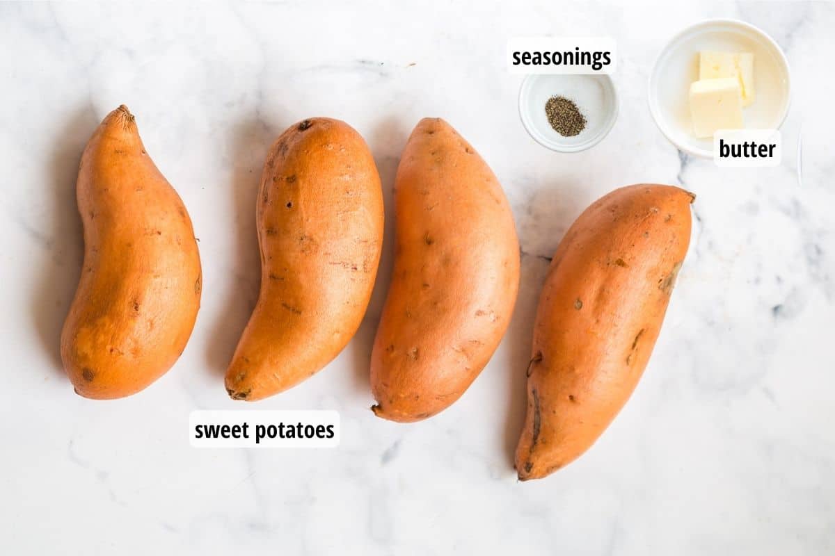 Marble counter top with four sweet potatoes and two white bowls filled with butter and seasonings.