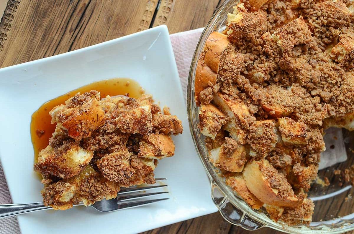 A circular glass baking dish of french toast casserole with a slice removed and set on a white plate with a fork.