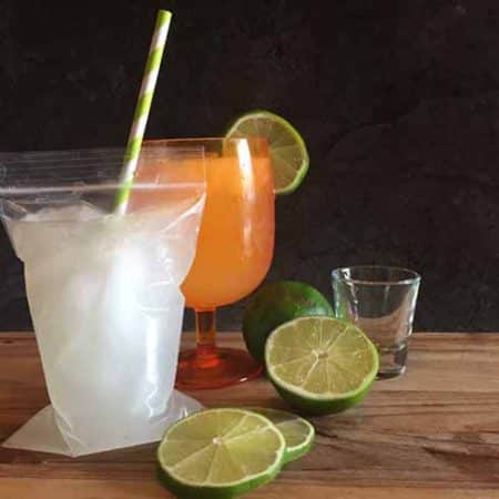 Margarita pouch with straw on a wood cutting board. There are sliced limes next to the drink.