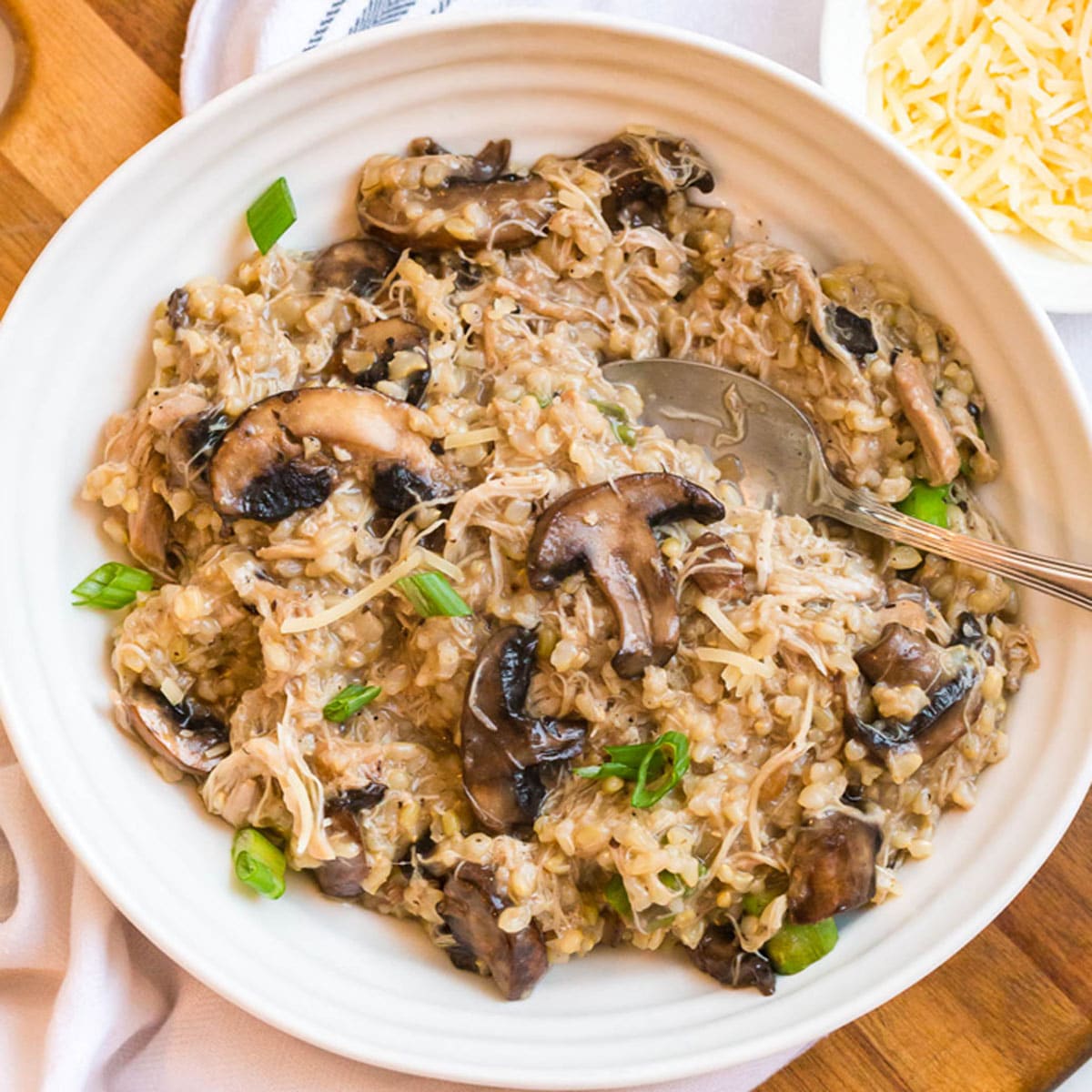 White bowl with chicken mushroom risotto and a wood charger underneath. 
